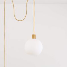 a white and gold light hanging from a long golden cord on a wall in a room