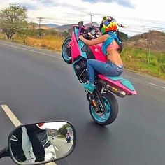 a woman riding on the back of a pink motorcycle next to a side view mirror