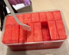 a plastic container filled with watermelon cubes and a fork sticking out of it