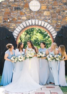 a group of women standing next to each other in front of a stone wall and archway