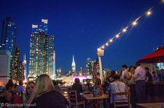 many people are sitting at tables in front of the cityscape and lights that hang above them