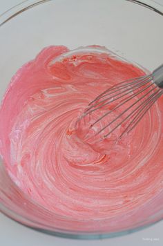 a mixing bowl filled with pink icing and whisk