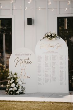 a wedding ceremony sign with flowers and greenery in front of a white barn door