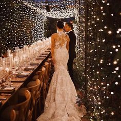 a bride and groom standing next to each other in front of a long table covered with candles