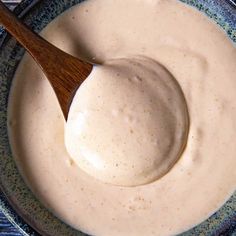 a wooden spoon in a blue bowl filled with white sauce on top of a table