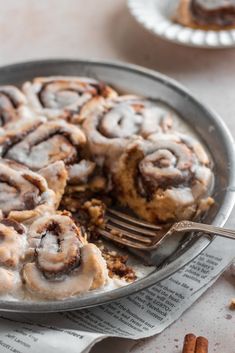 cinnamon rolls with icing on top in a pan next to a fork and napkin