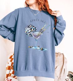 Celebrate your love for skiing and après ski festivities with this chic and playful sweatshirt! Featuring a stylish martini glass with crossed skis and a disco ball, this design embodies the fun and relaxation of après ski moments. Perfect for ski enthusiasts and cocktail lovers alike, this sweatshirt will keep you warm and stylish whether you're lounging by the fire after a day on the slopes or heading to a winter party. Crafted from soft, cozy fabric, this sweatshirt is ideal for layering during ski season or for casual winter wear. How To Order 1. Please, check and review all photos. 2. Select your Sweatshirt size and color. 3. Click add to cart. Continue shopping for free shipping! ($35 minimum) 4. If finished, Click "Proceed to check out" to finalize.  5. Carefully review all items as Long Sleeve Ski Tops For Ski Season, Long Sleeve Skiing Tops For Ski Season, Casual Winter Skiing Tops, Long Sleeve Sweatshirt For Winter Sports, Long Sleeve Tops For Ski Season And Winter Sports, Long Sleeve Tops For Ski Season, Casual Skiing Tops, Casual Crew Neck Sweater For Ski Season, Casual Graphic Print Tops For Winter Sports