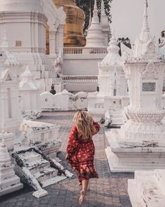 a woman in a red dress is walking through an area with white buildings and pagodas