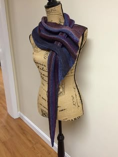 a mannequin wearing a purple and blue scarf on top of a wooden stand