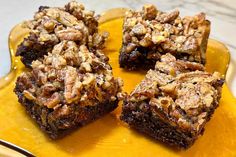 some brownies are on a yellow plate and have walnuts in the top one