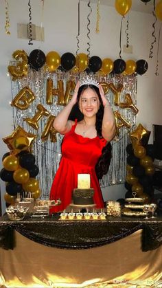 a woman in a red dress standing behind a table with gold and black balloons on it