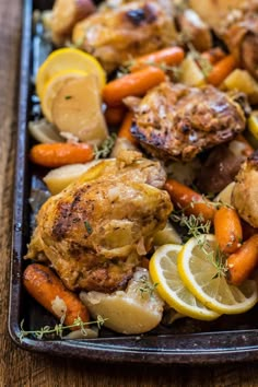 chicken, carrots and potatoes on a baking sheet with lemon wedges in the middle