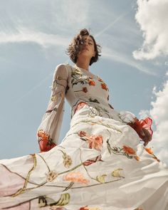 a woman in a long white dress is standing on the ground and looking up into the sky