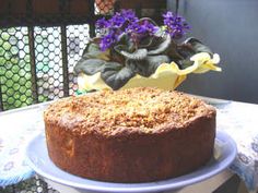 a cake sitting on top of a white plate next to a potted plant with purple flowers