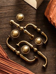 four brass handles on a wooden table next to an open book and some tassels