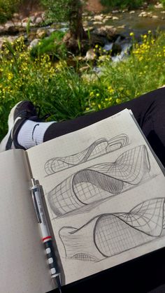 a person holding a notebook and pen in their lap while sitting next to a river