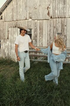 a man and woman holding hands walking in front of a barn with an old building