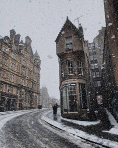 two people walking down a snowy street in the middle of winter with buildings on either side