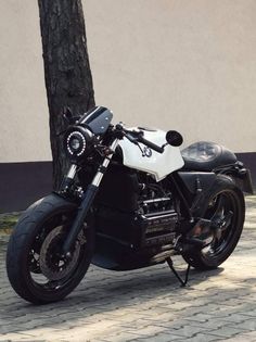 a black and white motorcycle parked next to a tree on a brick road in front of a building