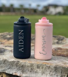 two personalized water bottles sitting on top of a stone slab in front of a golf course