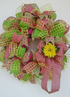 a pink and green wreath with a yellow flower on the front, sitting on a white surface