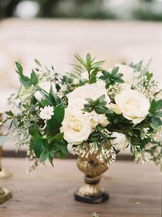 a vase filled with white flowers sitting on top of a wooden table next to candles