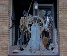 two skeletons are standing on the front steps of a house, one is holding a steering wheel