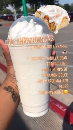 a person holding up a drink with whipped cream and cinnamon rolls on it's side