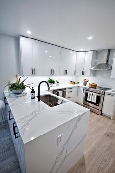 a white kitchen with marble counter tops and stainless steel appliances in the center, surrounded by wood flooring