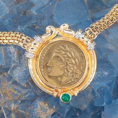 This gorgeous Robert Bartholomew designed pendant is centered with an Italian gold toned base metal token. The token depicts on the obverse with a Roman woman in profile wearing a leaf headdress, earrings and a beaded necklace. The reverse of the token depicts a soldier scene. The frame of the pendant is accented with one (1), bezel set, round cabochon cut natural emerald and twelve (12), bead set, round brilliant cut diamonds. The pendant measure 30mm wide and is attached to a 14k yellow gold fancy link neck chain measuring 5mm wide and an overall length of 16 inches. There are matching earrings for this necklace and the SKU number is A93748. Woman In Profile, Diamond Pendant Sets, Bead Set, Medallion Necklace, Neck Chain, Natural Emerald, Gold Design, Pendant Set, Round Brilliant Cut Diamond