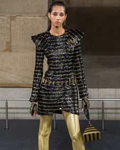 a model walks down the runway in gold and black