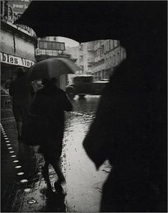 black and white photograph of people walking in the rain with umbrellas