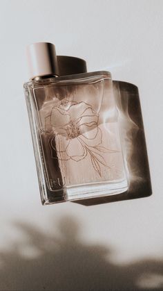 a bottle of perfume sitting on top of a white table next to a shadow cast object