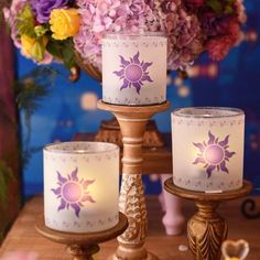 three candles are sitting on a table with flowers in the background