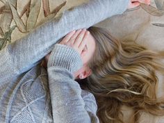 a woman laying on top of a bed next to a pillow covered in blankets and sweaters