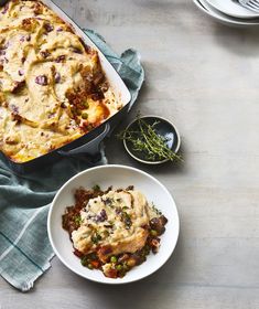 a casserole dish with meat and vegetables next to a bowl of mashed potatoes