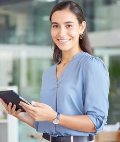 a woman in a blue shirt is holding a tablet computer and smiling at the camera