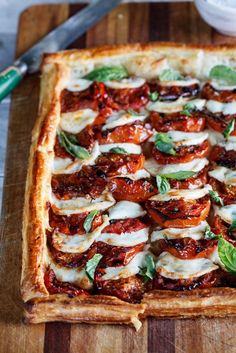 a square pizza with tomatoes and mozzarella on it, sitting on a wooden cutting board