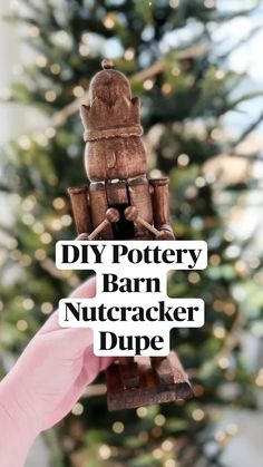 a hand holding up a wooden nutcracker in front of a christmas tree with the words diy pottery barn nutcracker dipe