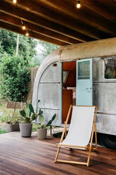 an old airstream sits on a deck with a lawn chair and potted cacti