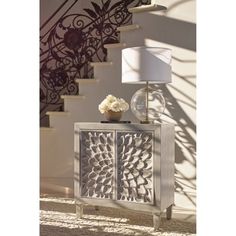 a white lamp sitting on top of a table next to a stair case and a vase with flowers