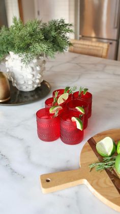 some red glasses are sitting on a table with limes and other fruit in the background