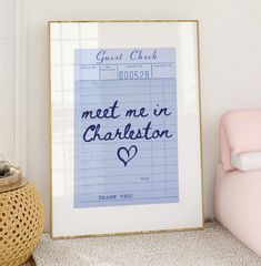 there is a framed poster with the words meet me in charleston on it next to a pink chair