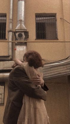 a man and woman embracing each other in front of a building with a large pipe