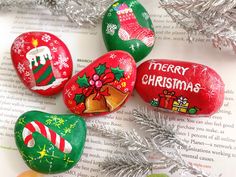 four painted rocks sitting on top of an open book next to christmas decorations and tinsel