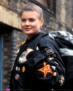 a woman in black jacket and backpack standing next to brick building with graffiti on it