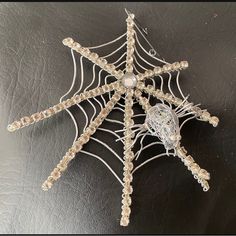 a spider web made out of beads on top of a black surface with a white and silver brooch