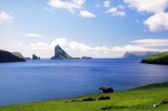 an island in the middle of a body of water surrounded by green hills and grass