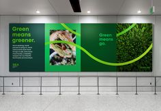 an empty subway station with two large green posters on the wall and people walking by