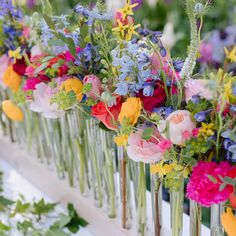 colorful flowers in vases lined up on a long table with greenery behind them